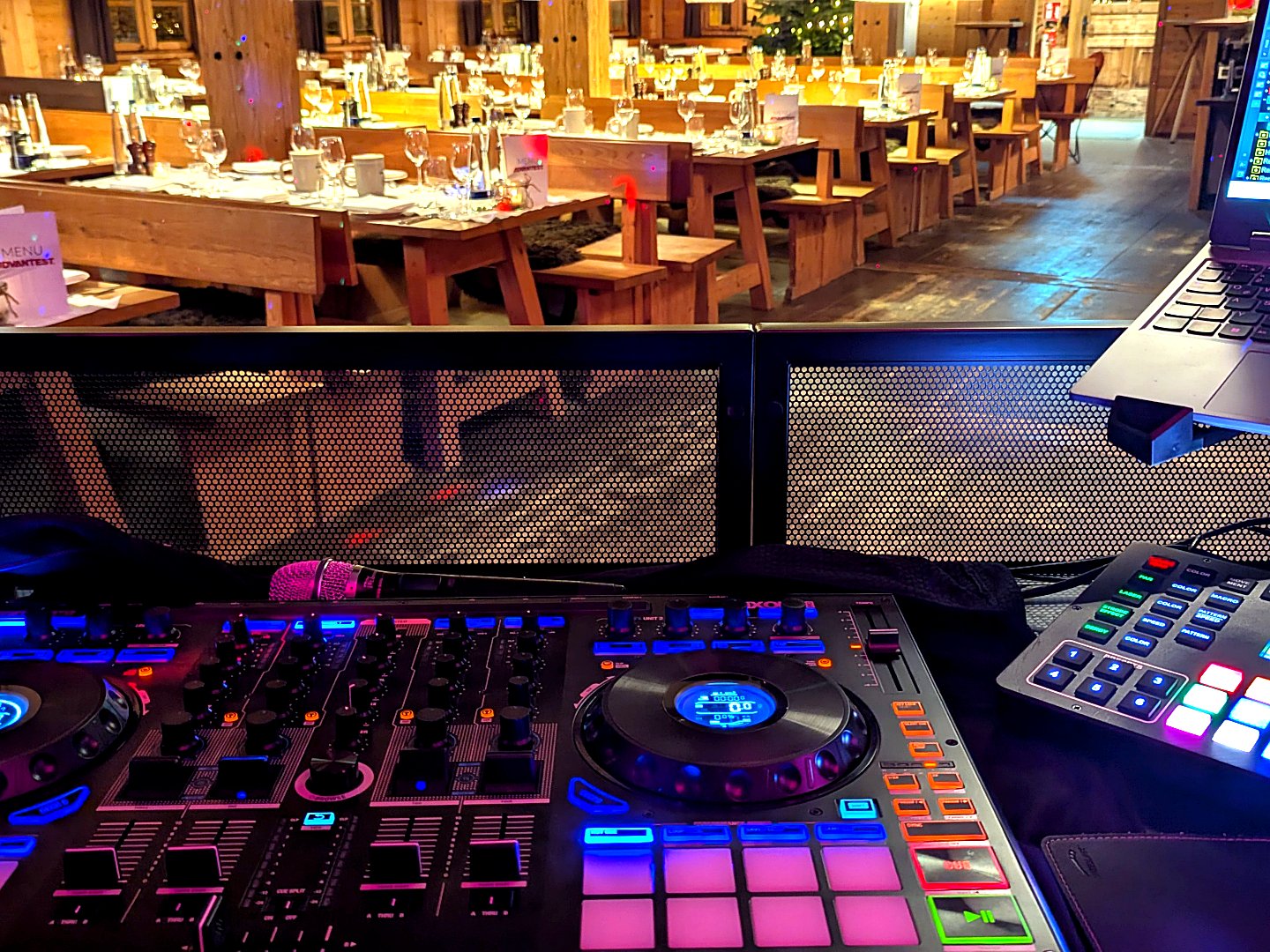 DJ-Pult mit bunter Beleuchtung vor festlich gedeckten Tischen in einer urigen Almhütte